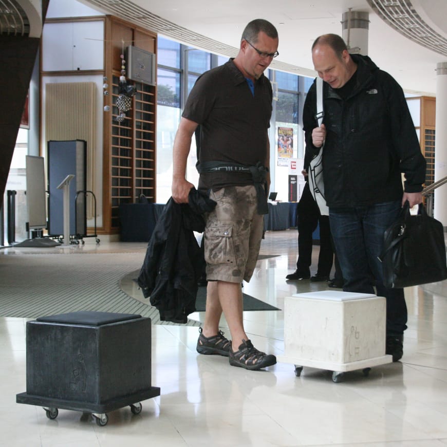 Two people look curiously at the grey and black concrete cubes