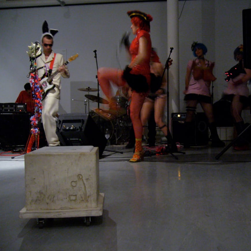 Grey concrete cube in the foreground of a punk gig