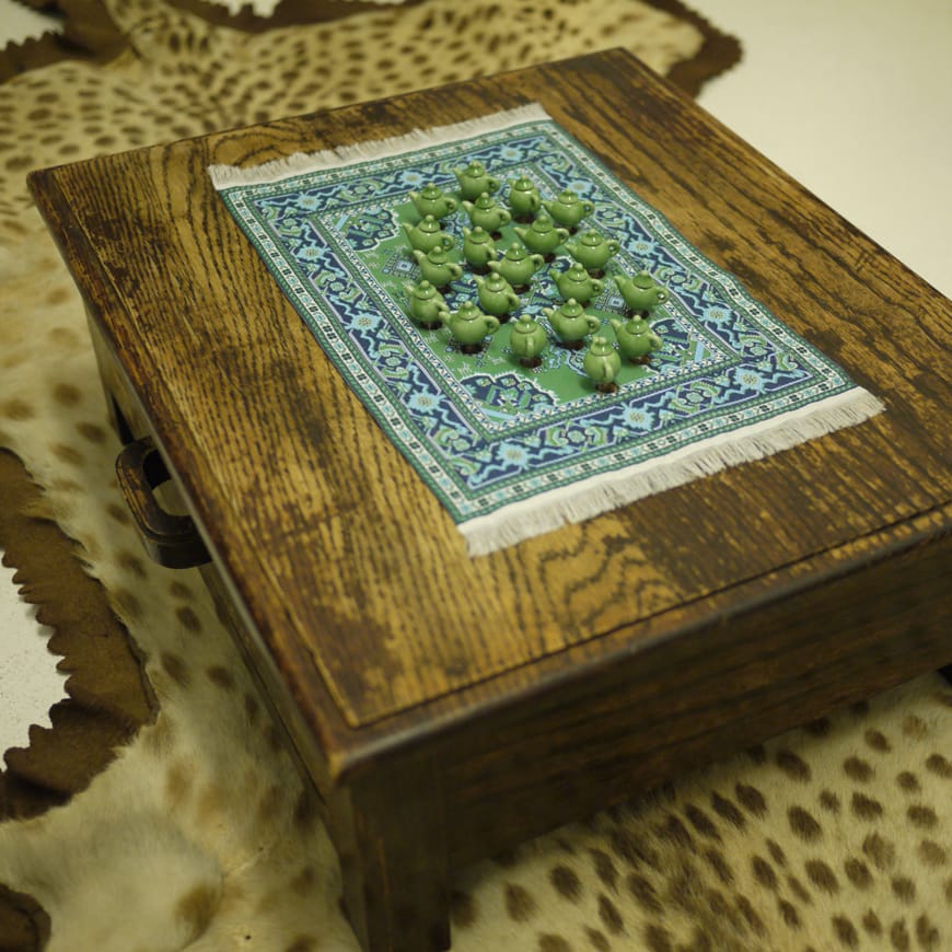 Tiny green teapots seen from above on top of miniature rug on a small wooden table