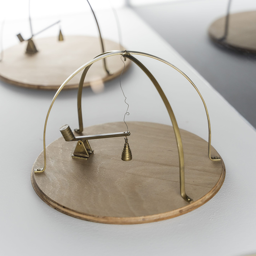 Kinetic sculpture made of a round wooden base with a small brass lever and a brass open cage